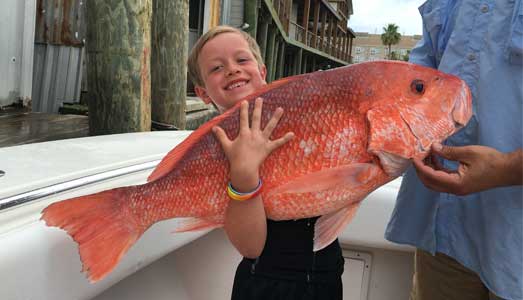 Young boy holds giant red snapper fish he caught on a Galveston deep sea fishing charter