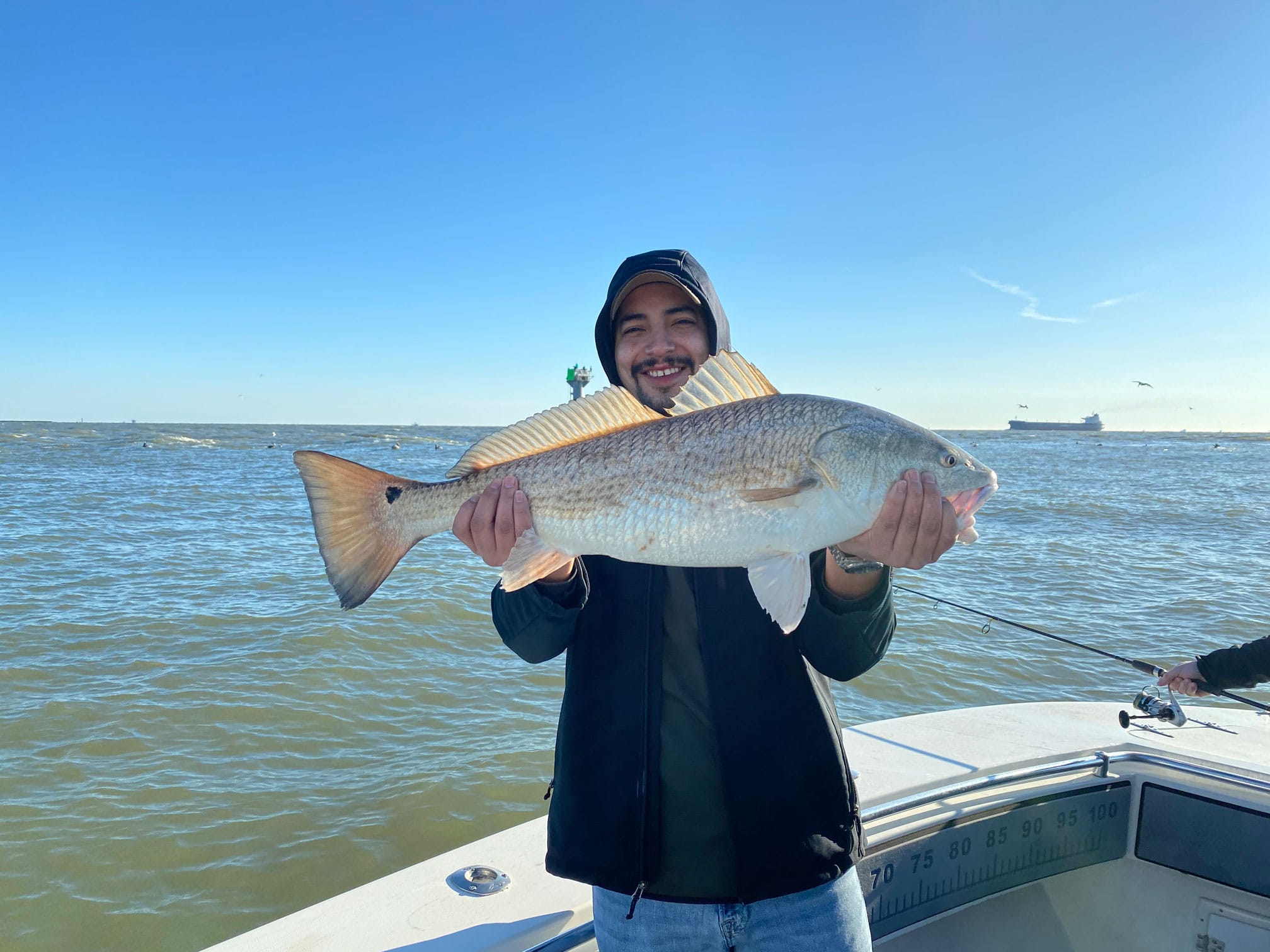 Man in hood smiling and holding fresh caught redfish