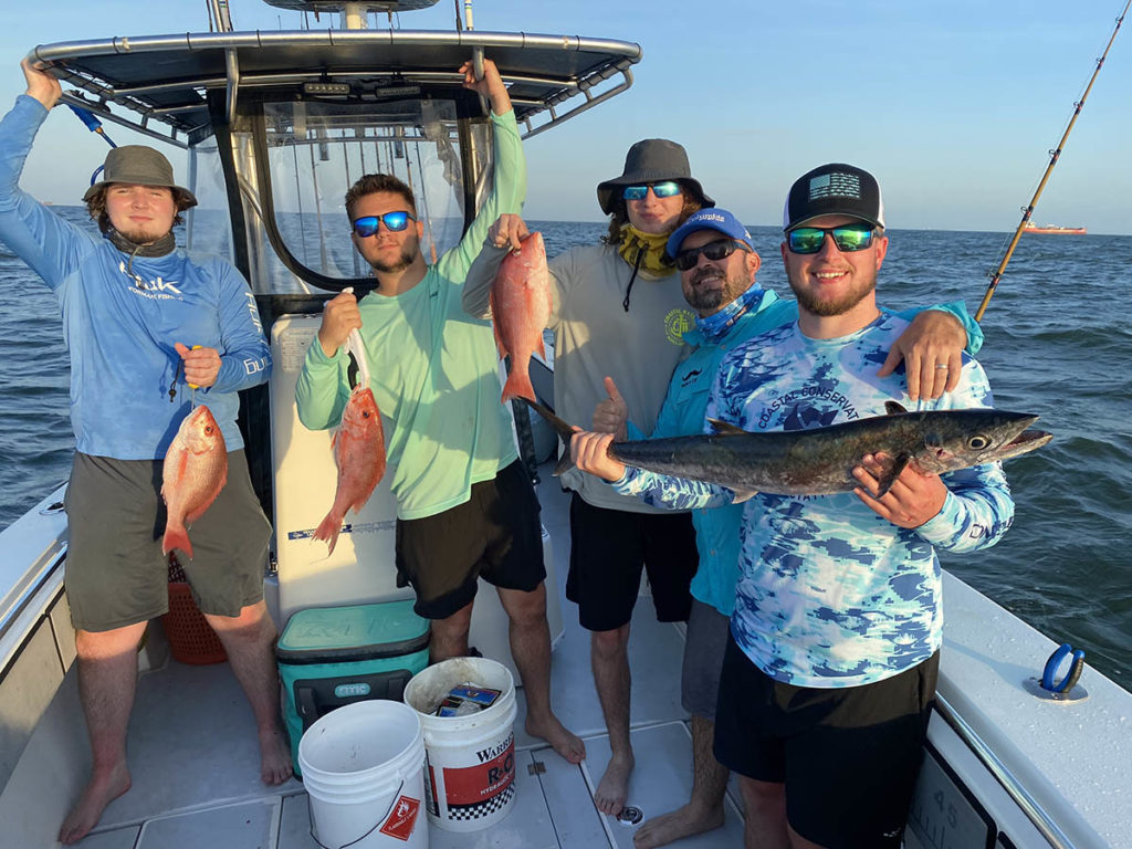 5 men on boat smiling and showing off the fish they caught in Galveston Bay