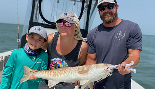 Family of three on a boat holding a redfish caught on a Galveston nearshore fishing trip.