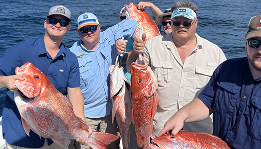 Five men on a boat all holding the fish they caught on a Galveston Red Snapper fishing trip.