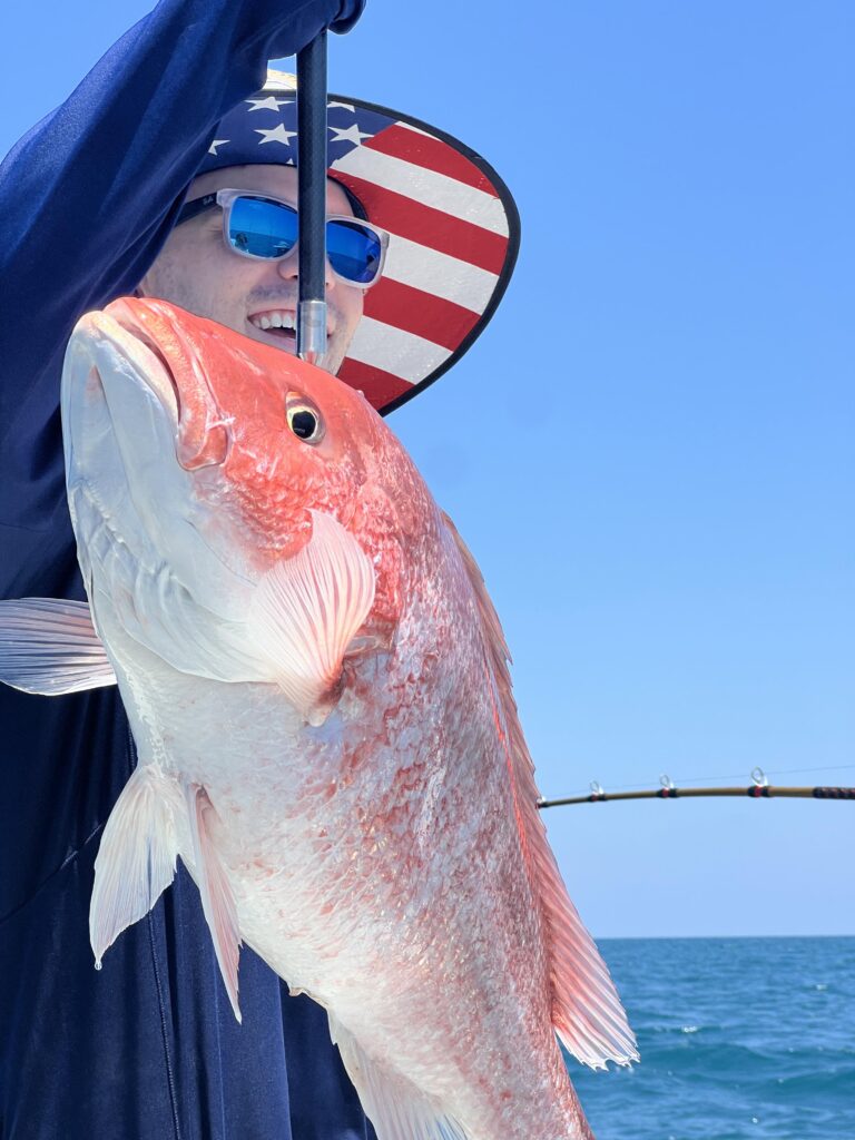 Man in American Flag hat holds up the Red Snapper he caught on a Galveston Fishing Charter.