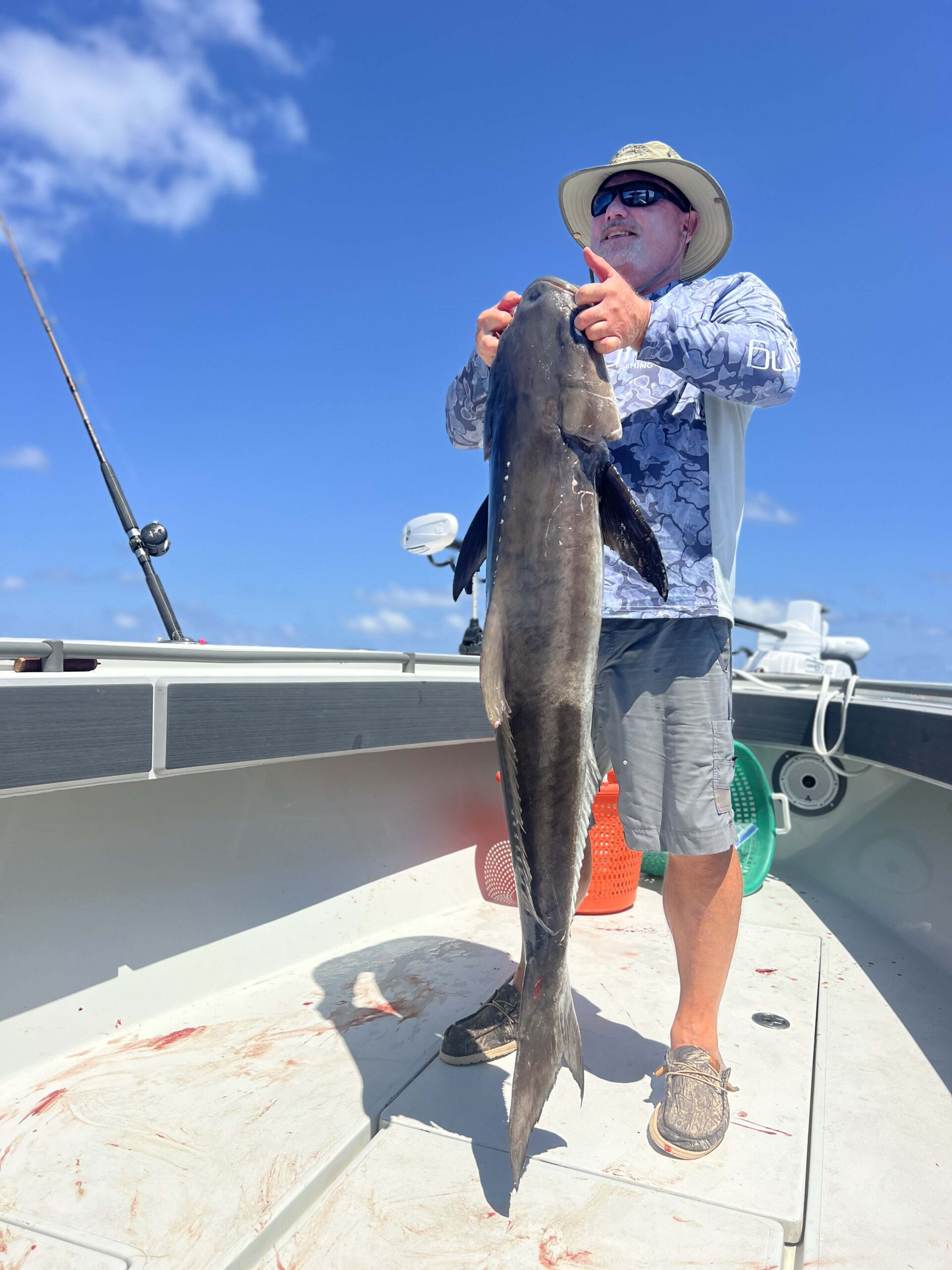 A man holds a large ling fish by the gills, aboard a Galveston Deep Sea Fishing boat.