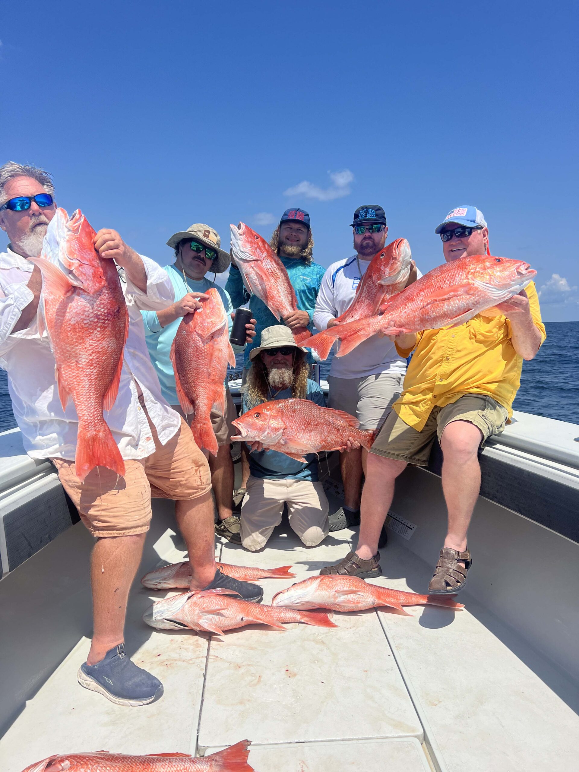 A large family poses on the bow of a boat, each holding a large red snapper they caught on a Galveston Fishing Trip.