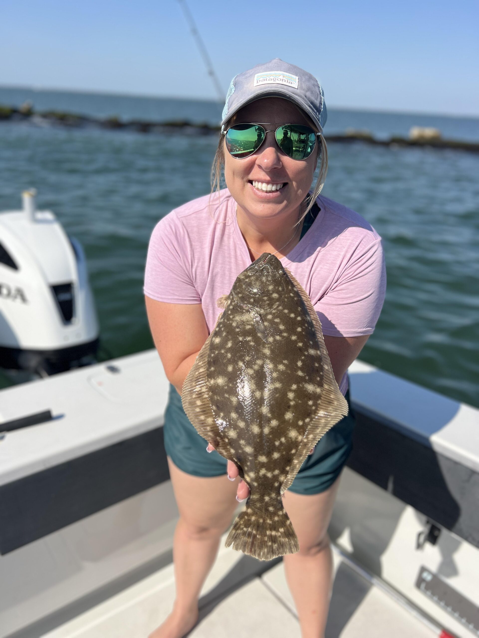 Young woman smiles while posing with the flounder she caught on a Galveston Bay & Jetty Fishing trip.