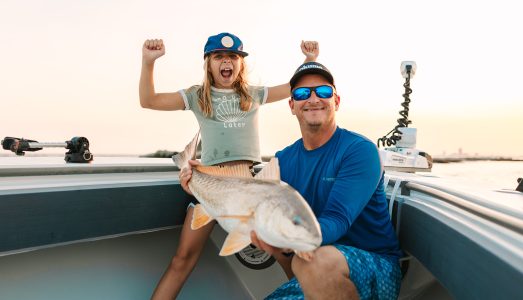 Young girl with her arms overhead, screaming with excitement about catching a large redfish on a Galveston Fishing Charter.