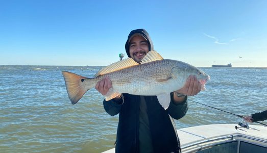 Man in hood smiling and holding fresh caught redfish